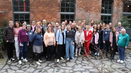 Menschen stehen für ein Gruppenbild vorm einem Gebäude.